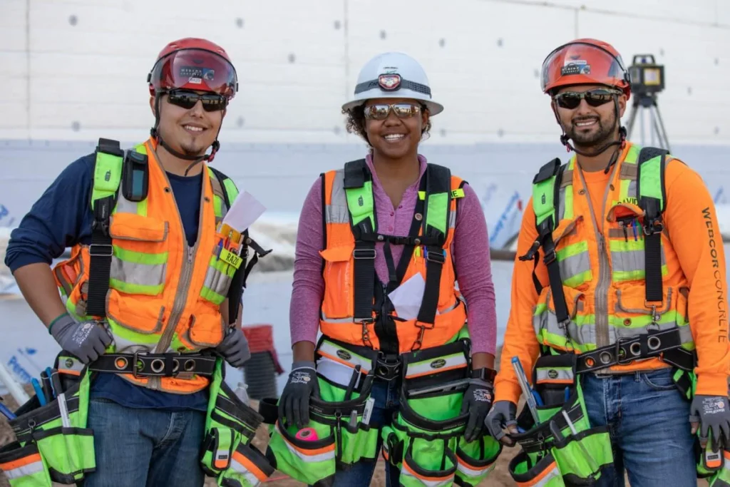 3 young construction workers smiling for camera, wearing protective gear