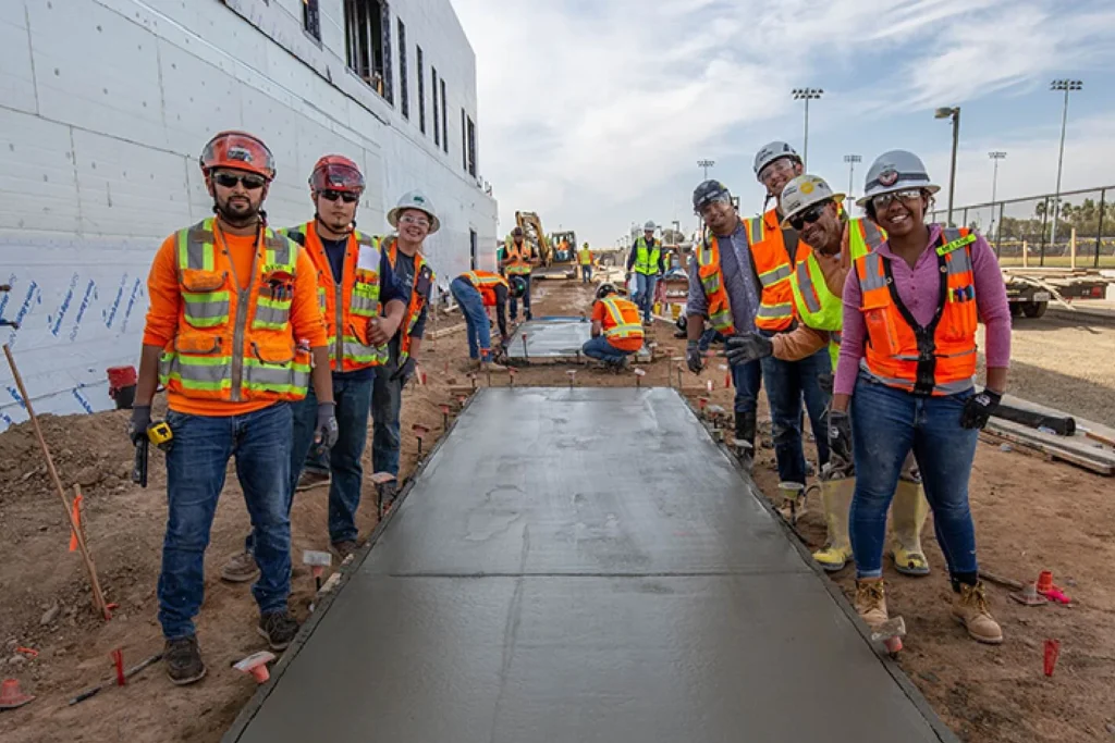 crew of construction workers standing around concrete sidewalk in the making